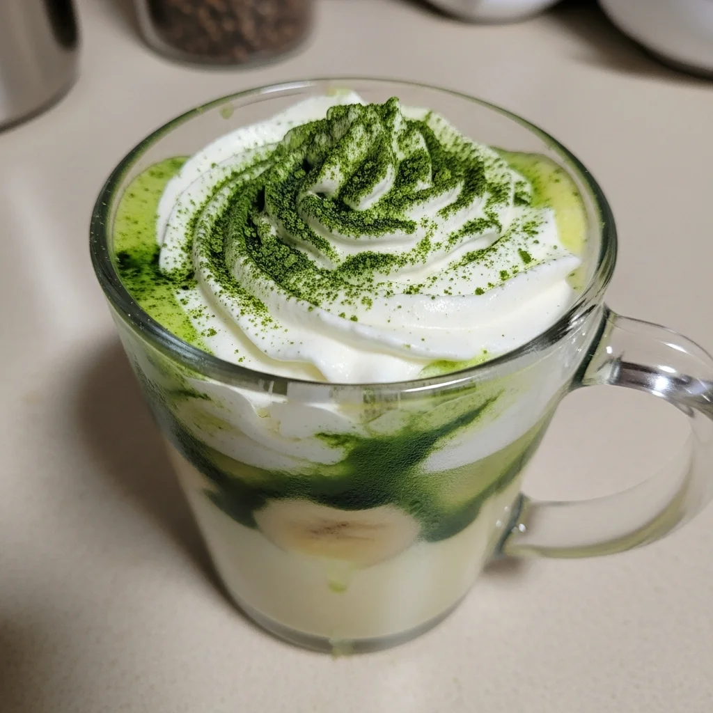 Taza de Latte de Plátano con crema y matcha decorada con espolvoreado verde.