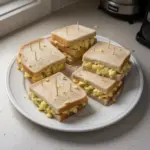 Mini sándwiches de ensalada de huevo sobre una tabla de madera.