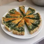 Quiche de espinacas y queso recién horneado en un plato, ideal para almuerzos.